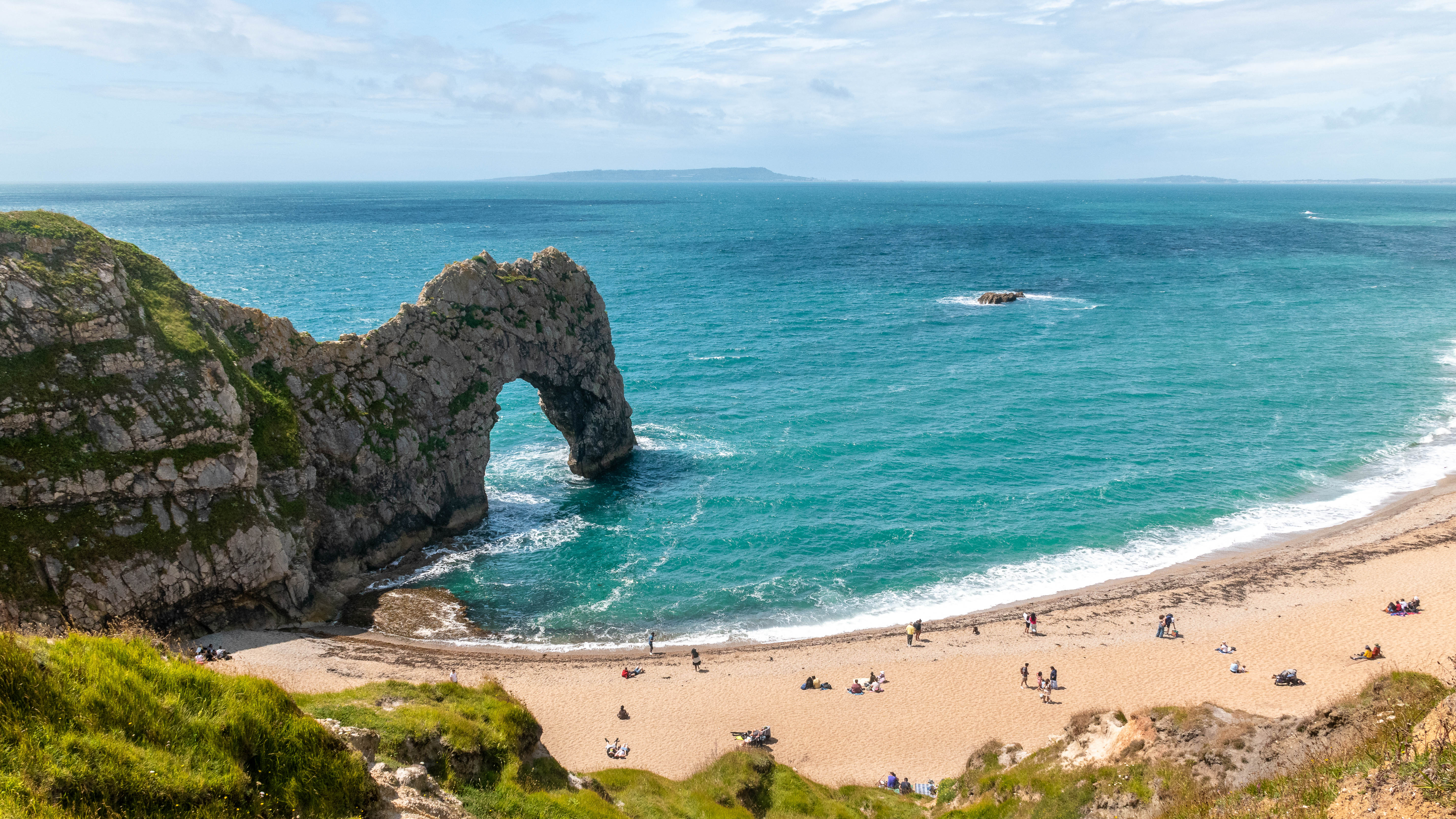 Stunning coastal view featuring a natural arch, sandy beach, and turquoise waters with visitors enjoying the scenery.
