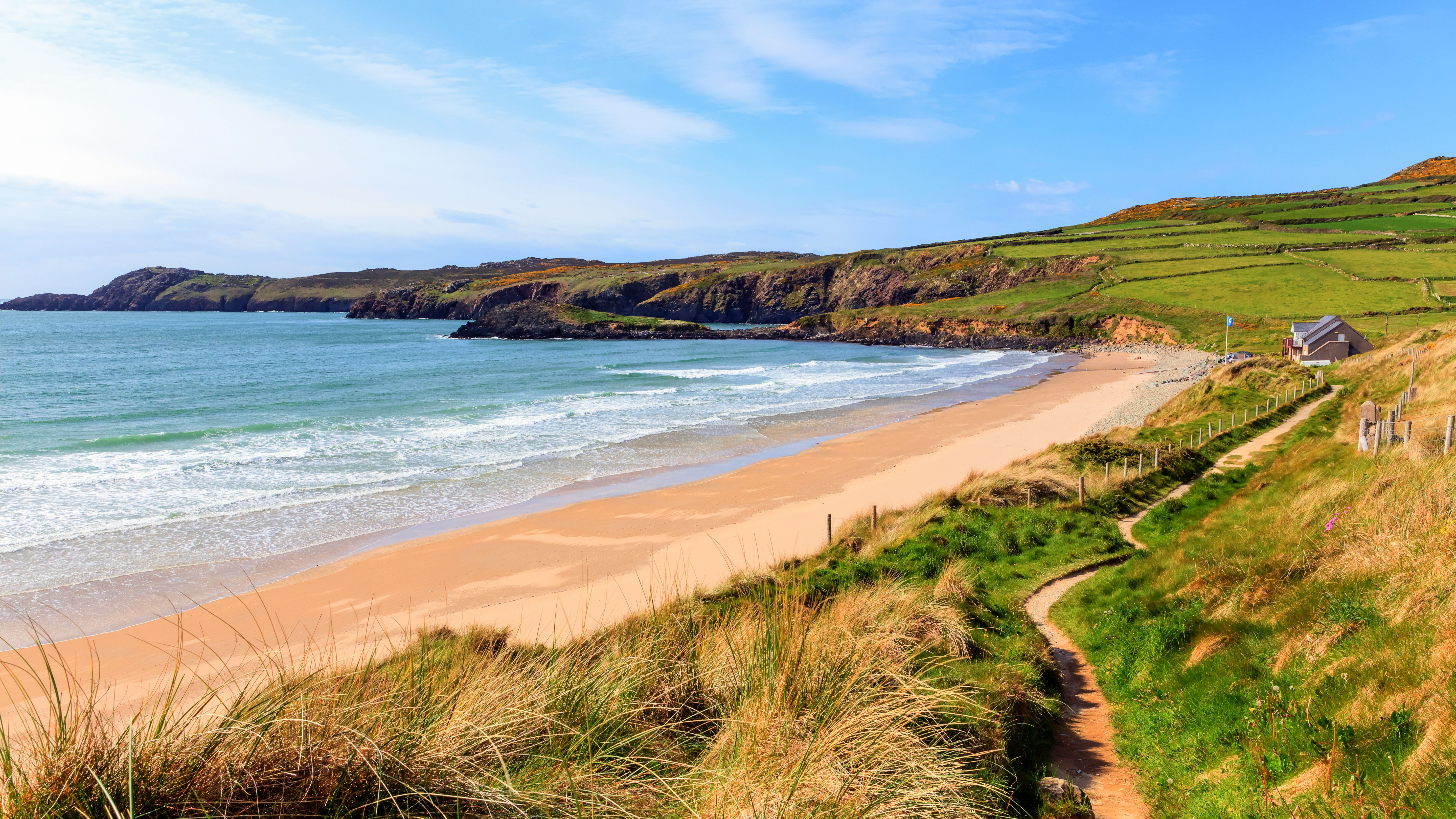 A serene beach scene with gentle waves, lush green hills, and a winding path leading to a cozy coastal house.