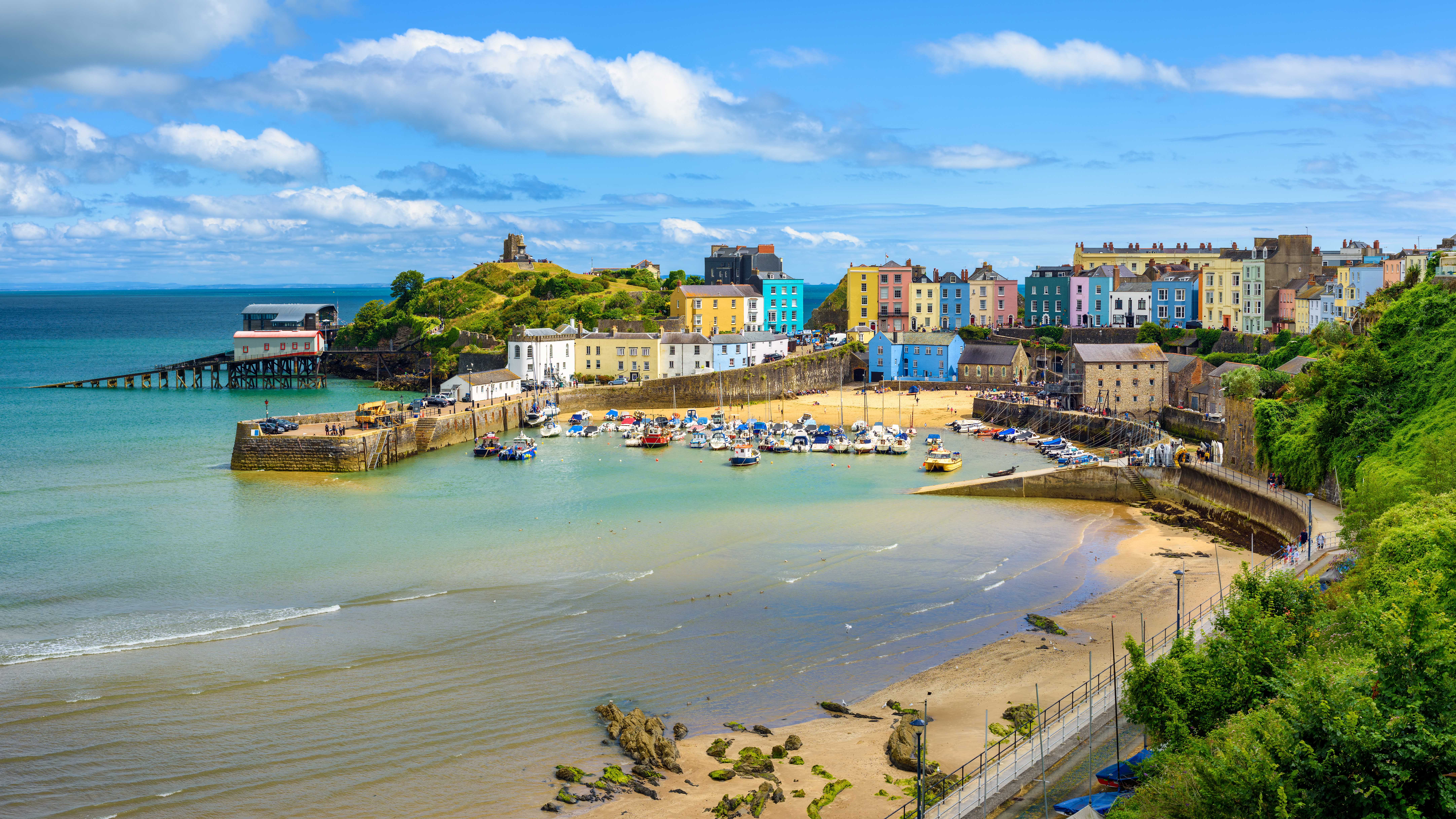 A picturesque coastal view featuring colorful buildings, a sandy beach, boats in the water, and a scenic landscape.