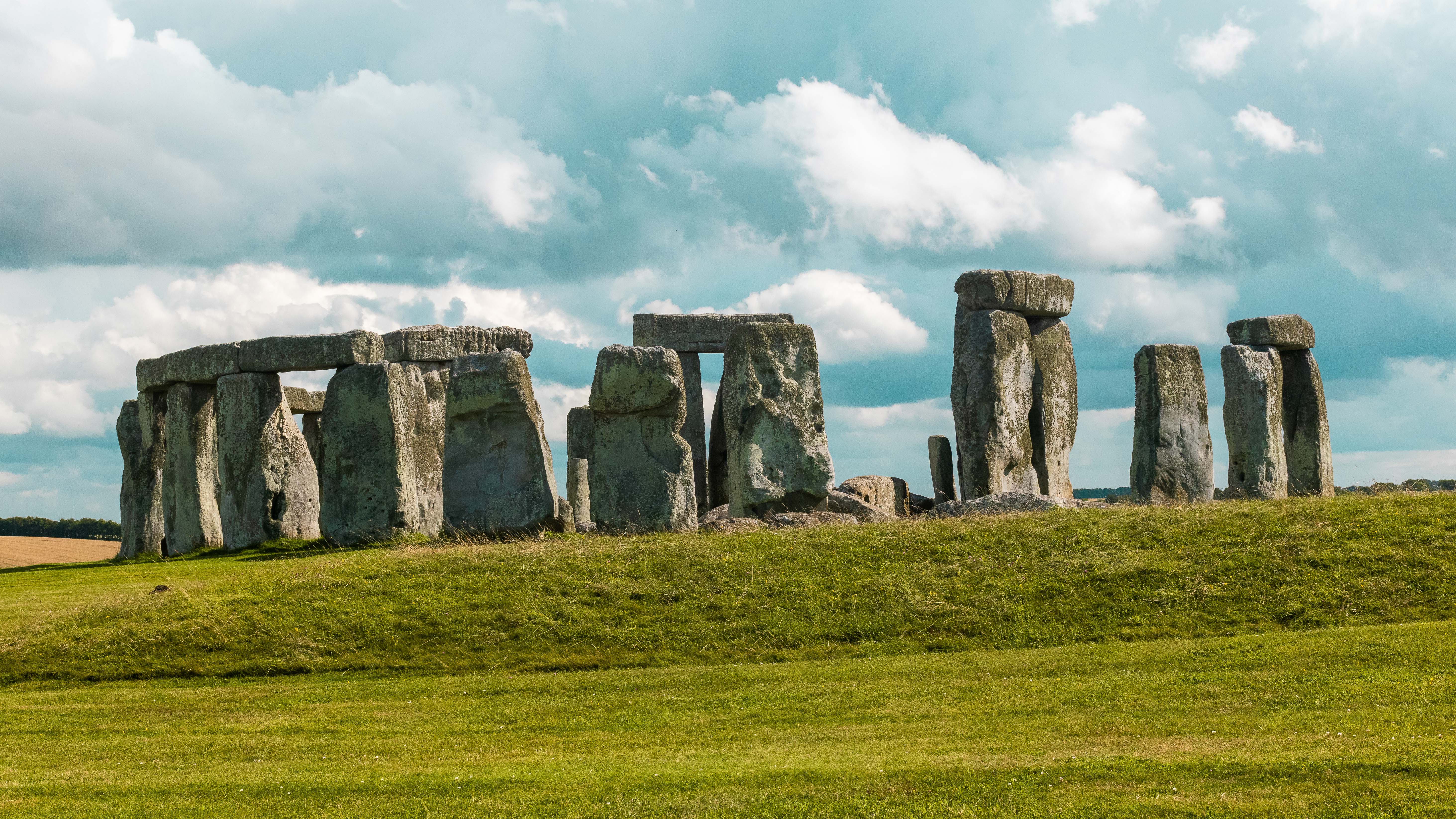 Historic Stonehenge, a prehistoric stone monument, stands majestically under a partly cloudy sky amidst green fields.