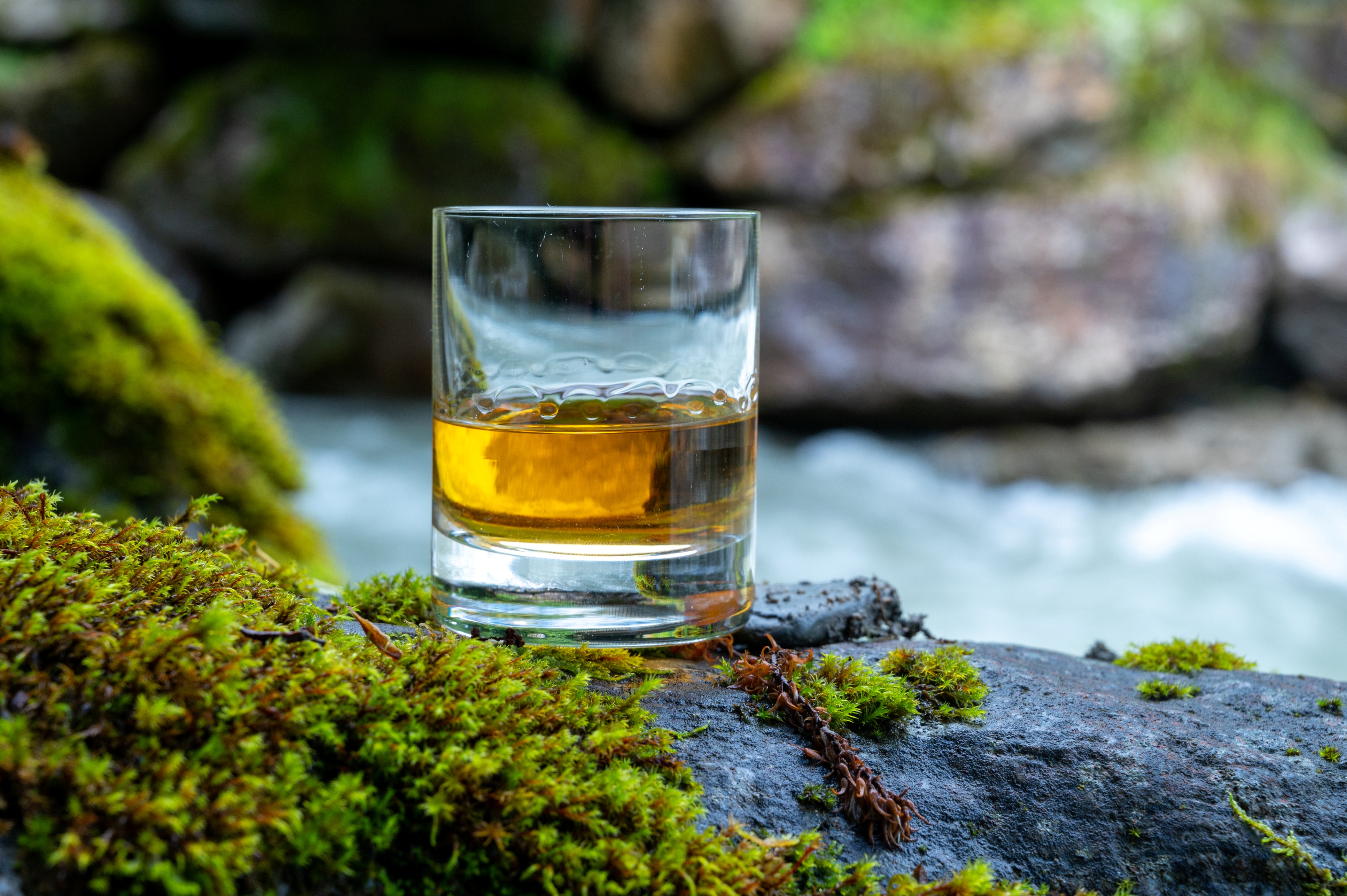 Glass of whisky on a rock by a fast flowing river