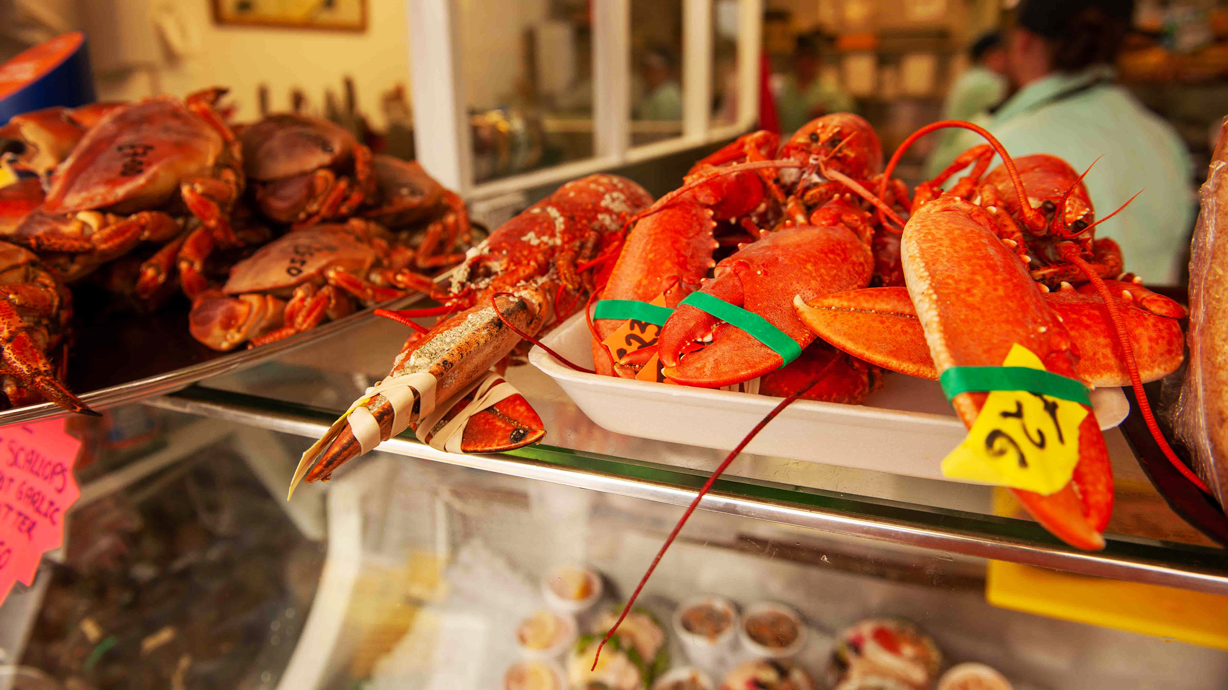Fresh seafood display featuring lobsters and crabs, bright colors and price tags visible in a bustling market setting.