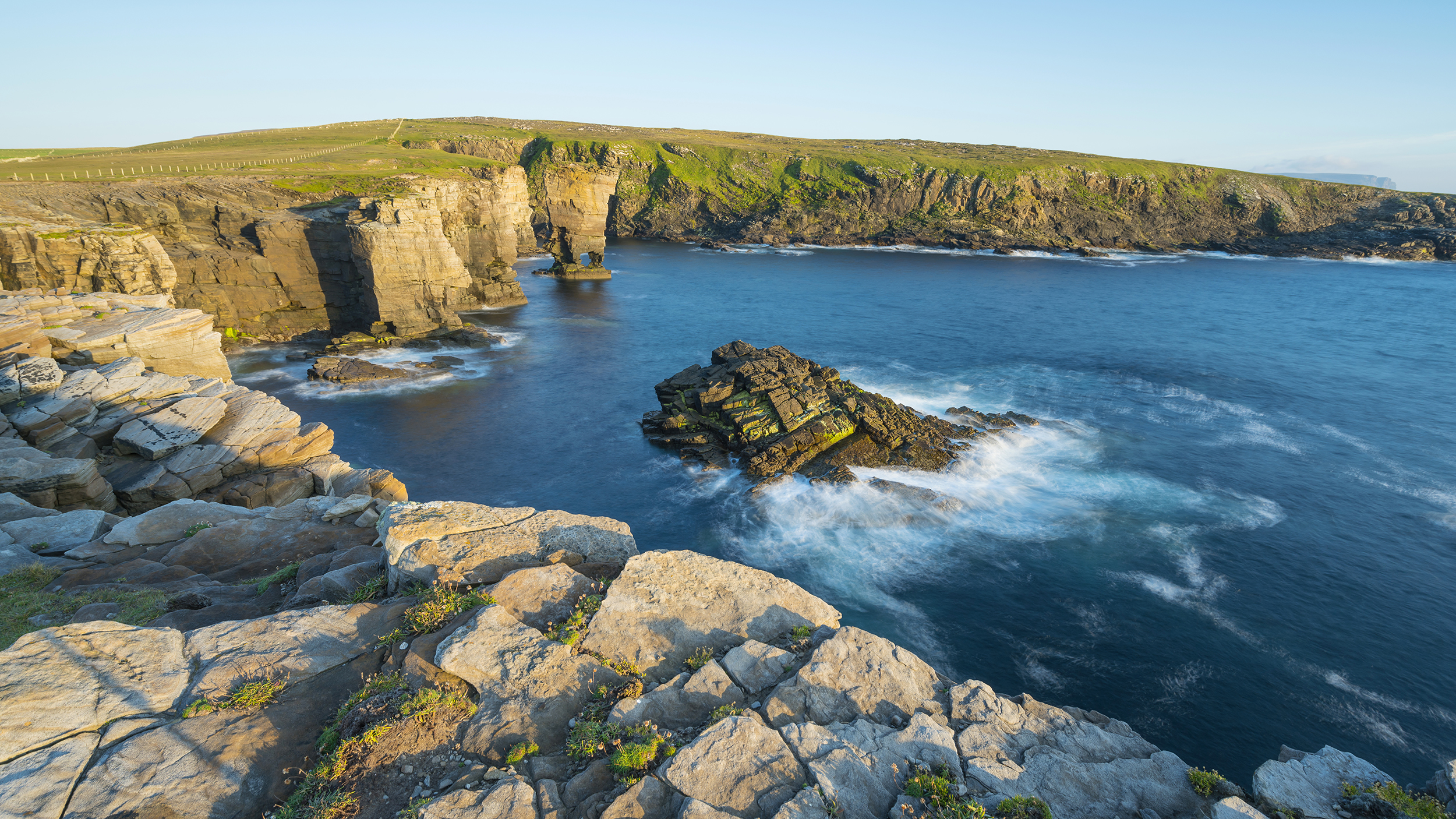 A scenic coastal landscape with rocky cliffs and calm blue waters, under clear skies, ideal for small group tours.