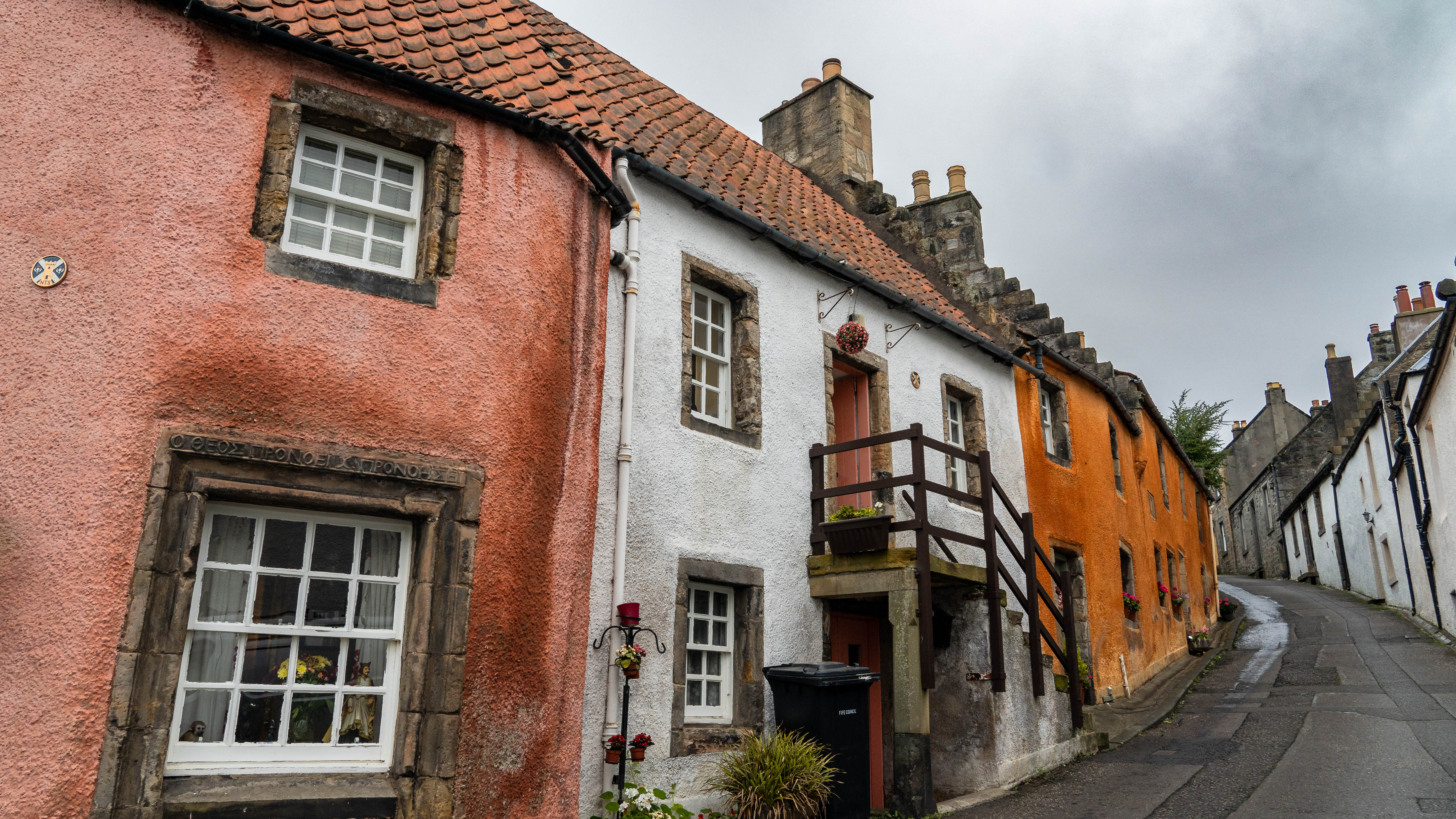 Charming colorful cottages line a narrow street under a cloudy sky, showcasing traditional British architecture.