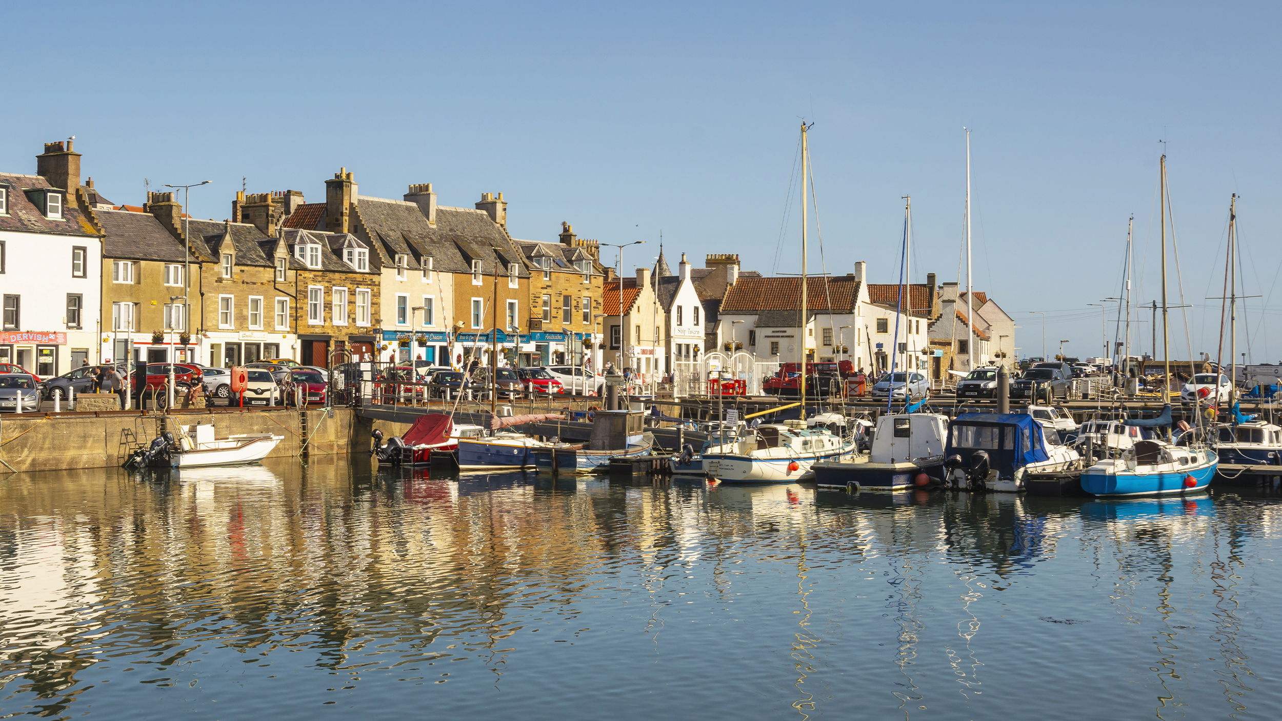 Picturesque harbor with colorful boats and charming buildings, reflecting on calm waters under a clear blue sky.