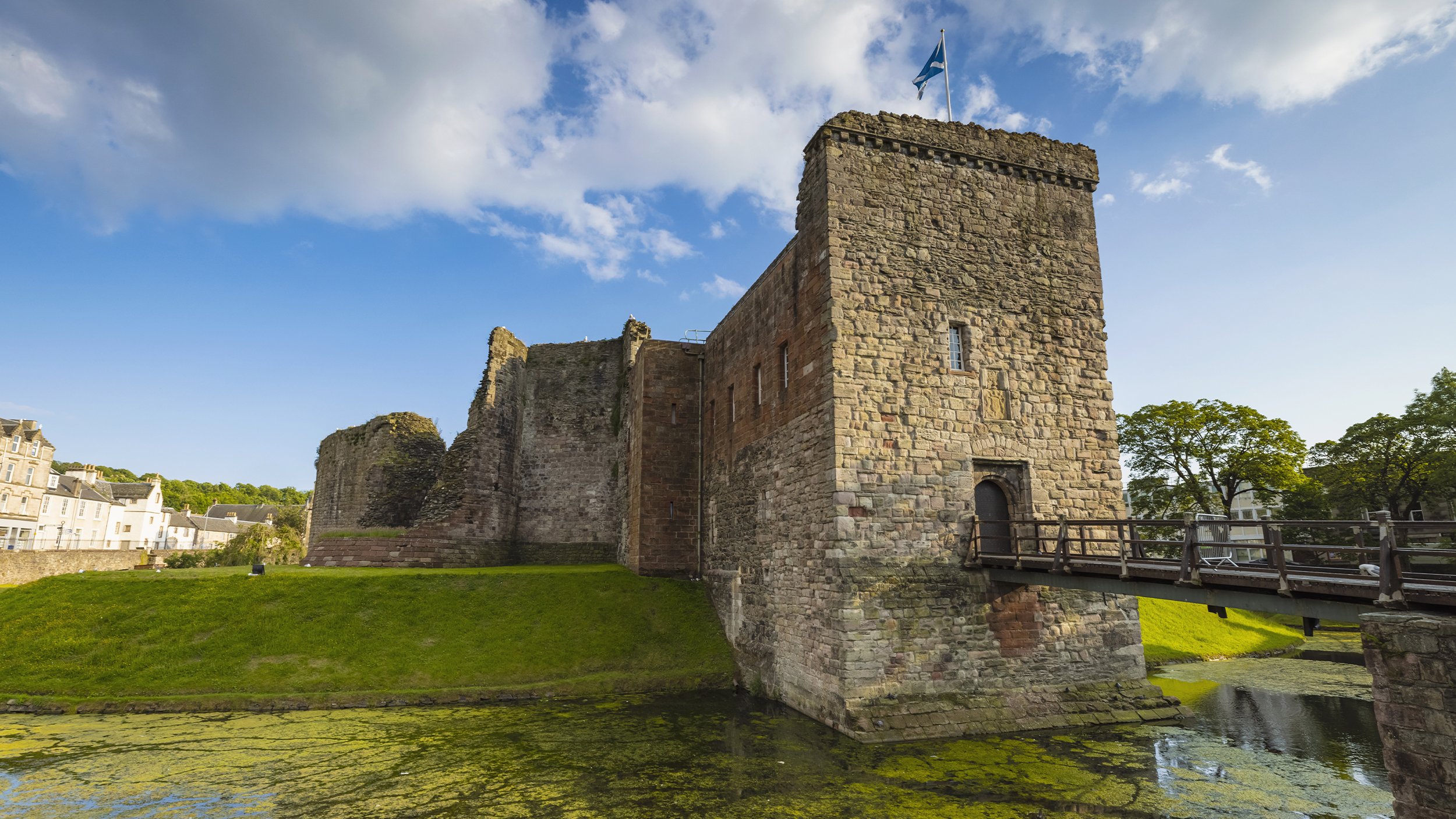 Historic stone castle ruins with a bridge, set against a blue sky and green surroundings, perfect for exploring UK heritage.