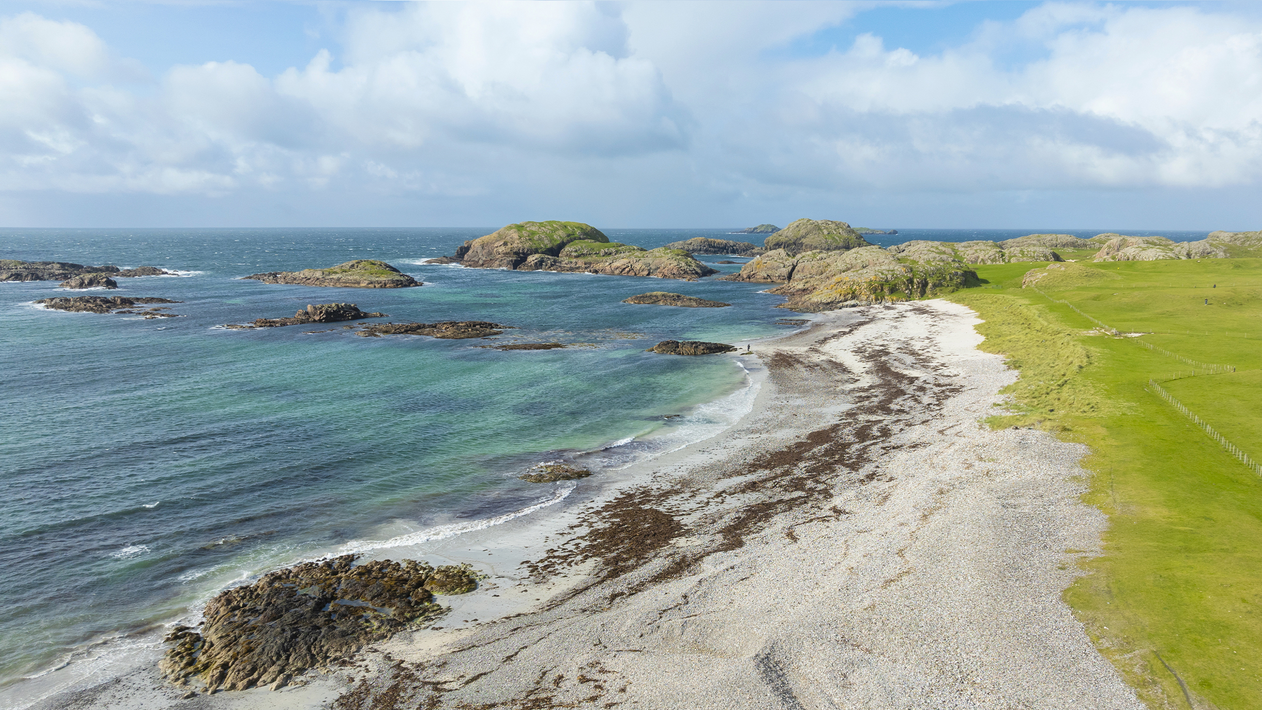 A scenic beach with calm waters, rocky islands, and lush greenery under a partly cloudy sky. Perfect for exploring!