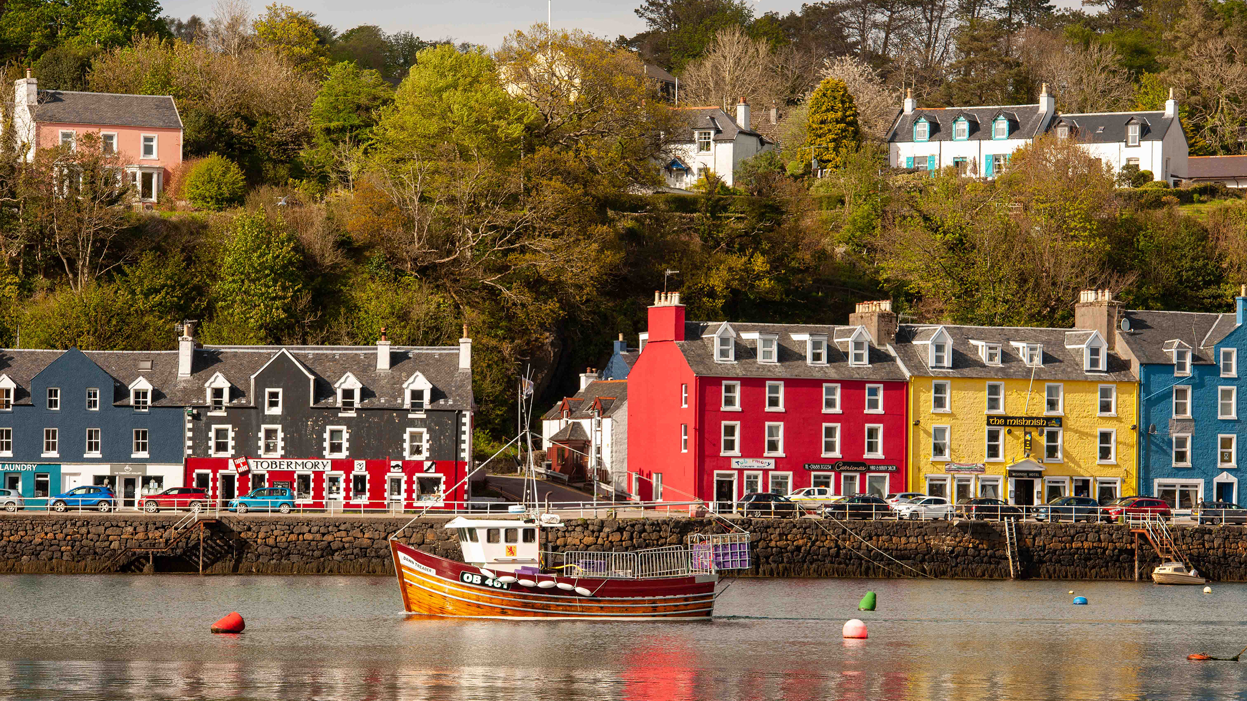 Colorful waterfront buildings and a fishing boat in Tobermory, showcasing the charm of the UK's coastal villages.
