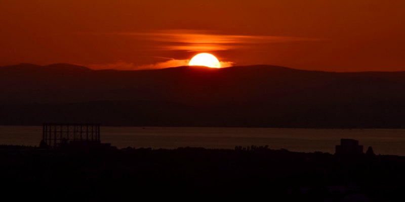 A stunning sunset over rolling hills, casting warm orange hues across the sky and reflecting on the tranquil water below.