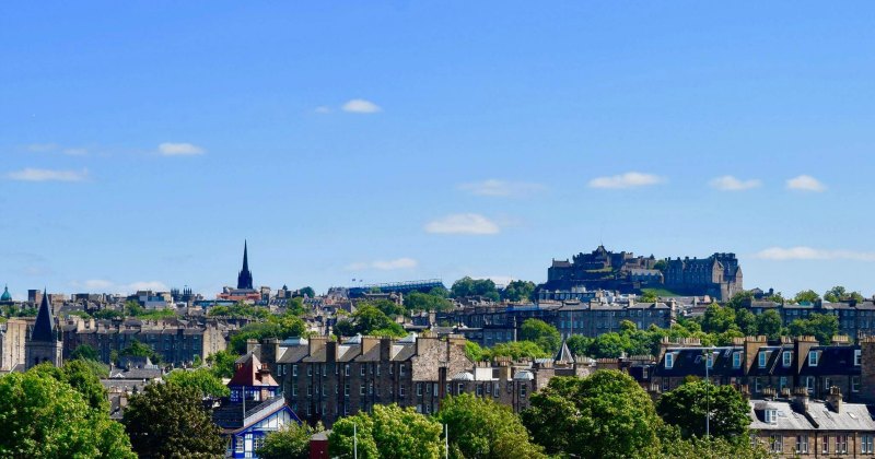 Edinburgh skyline featuring historic buildings and lush greenery under a clear blue sky. Ideal for exploring with Rabbie's Tours.