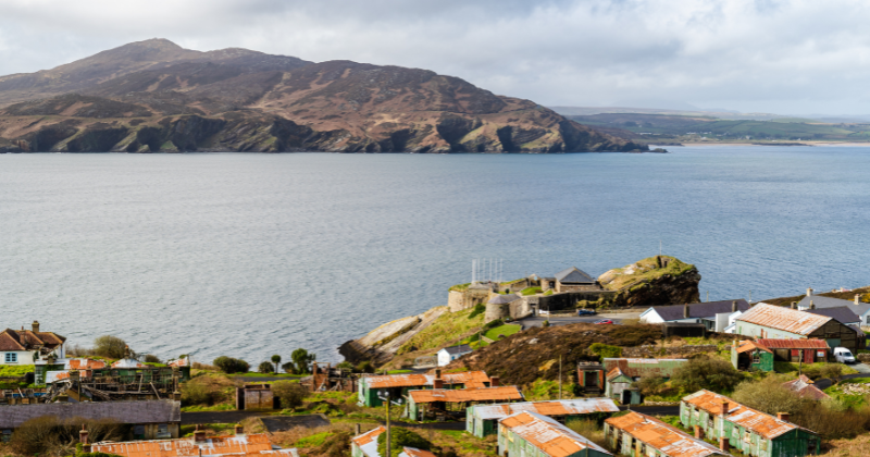 mountain in the background with the sea in the middle and a few houses on top of the cliff