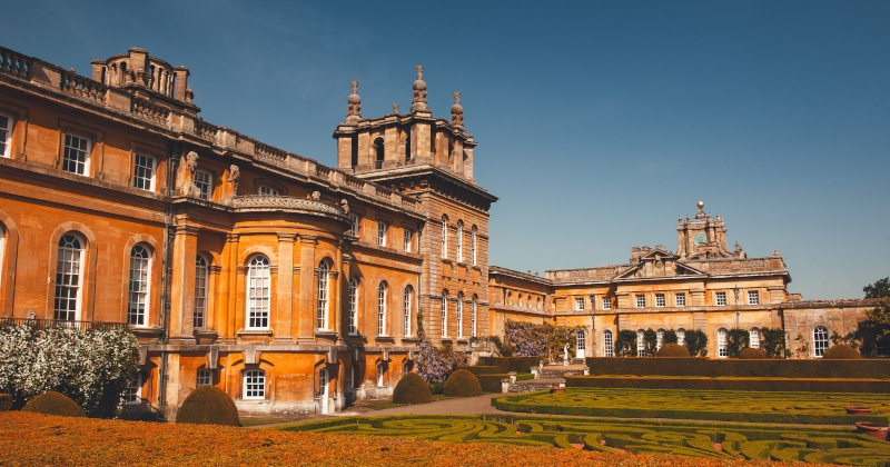 outer view of Blenheim Palace with a green maze in front and blue sky above