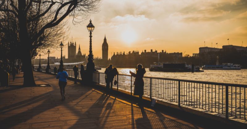 People standing beside a river next to a city at sunset