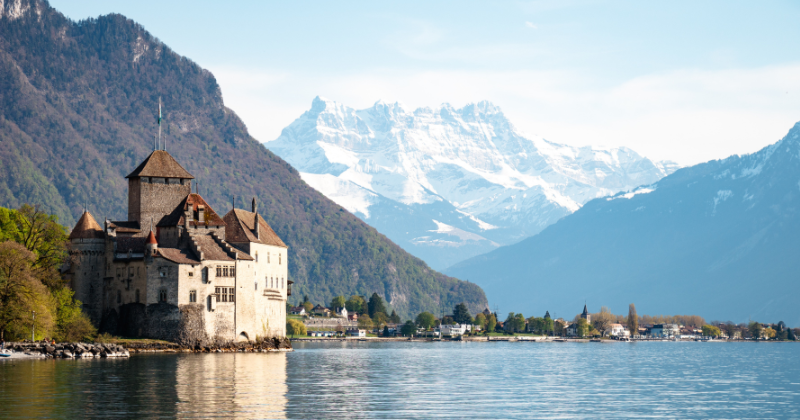 castle on the banks of a blue lake with snowcapped mountains behind