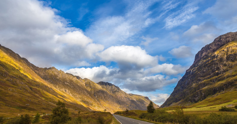 Scenic view of a winding road through mountains, showcasing lush greenery and dramatic skies in the UK.
