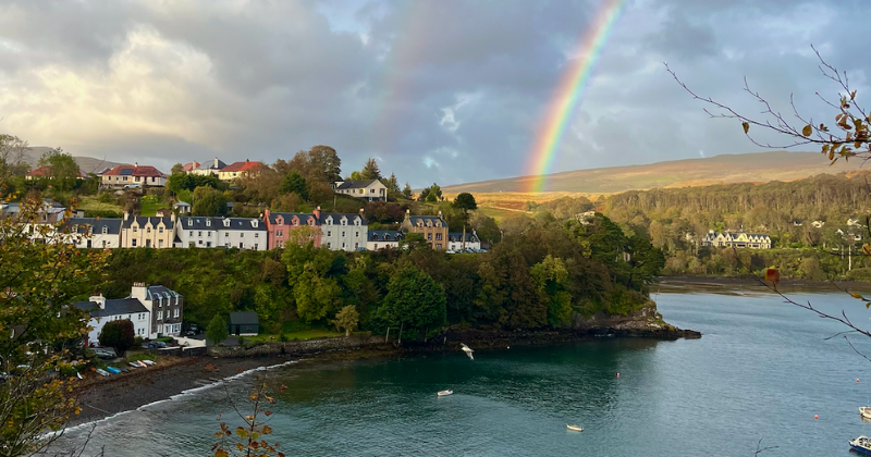 A row of houses overlooking a river with a rainbow overhead