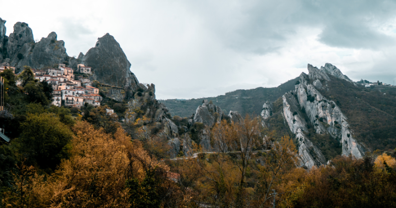 A picturesque view of rocky hills with a quaint village nestled among vibrant autumn foliage under a cloudy sky.