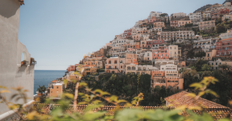 Colorful hillside buildings overlooking the sea, surrounded by lush greenery and a clear blue sky.