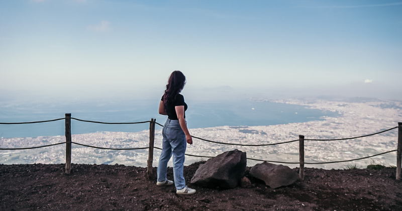 A person stands at a scenic overlook, gazing at a vast landscape under a clear sky.