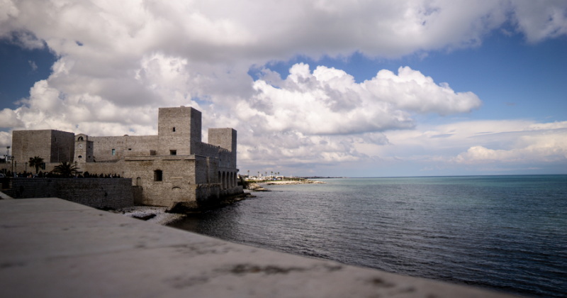 A scenic view of a coastal castle with calm waters and dramatic clouds, perfect for exploring historical UK landmarks.