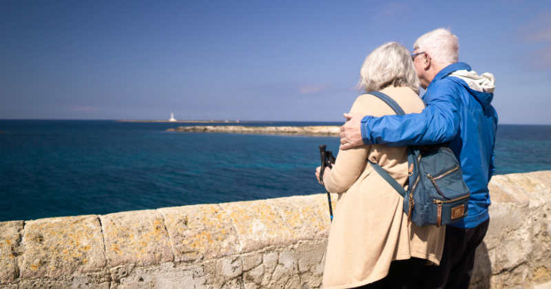 A couple stands by the sea, embracing while looking at the horizon, enjoying a scenic view.