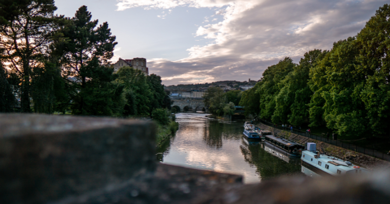 Scenic river view with boats, lush trees, and a historic bridge under a cloudy sky, showcasing the charm of the UK.