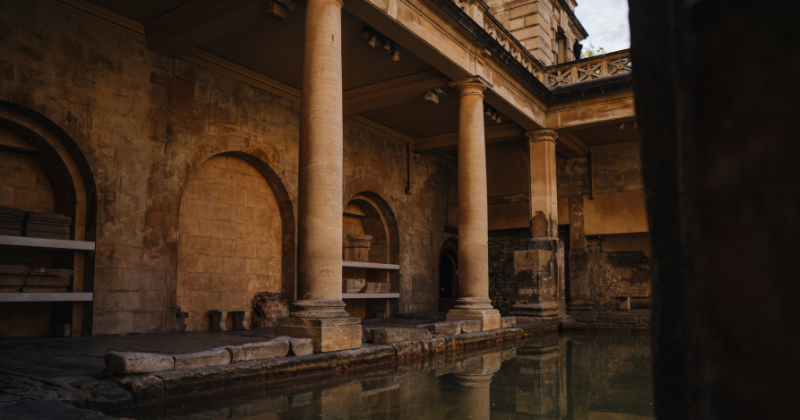 Ancient Roman bathhouse with stone columns and tranquil water reflecting the historic architecture.