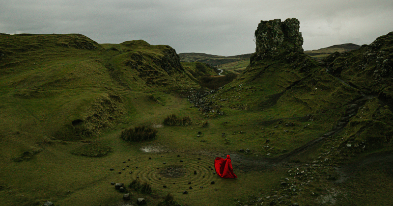 A person in a red cape dancing around a stone circle