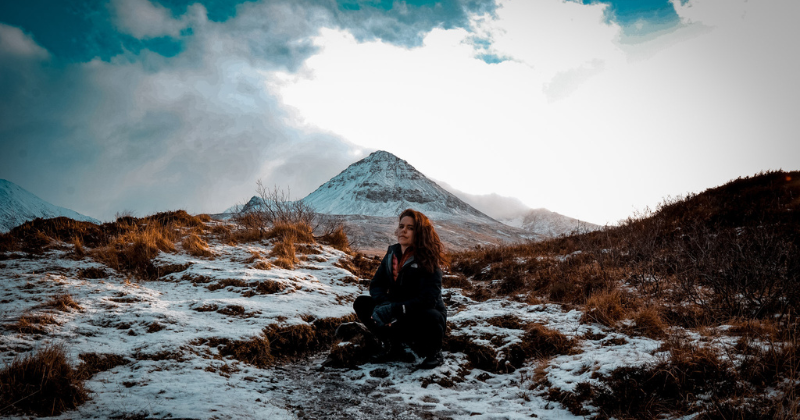 girl crouching in the snow in front of a mountain