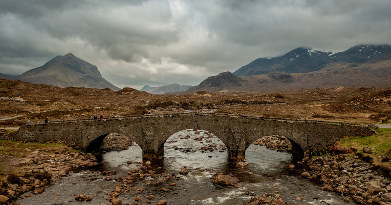 An old stone bridge over a river with mountains behind