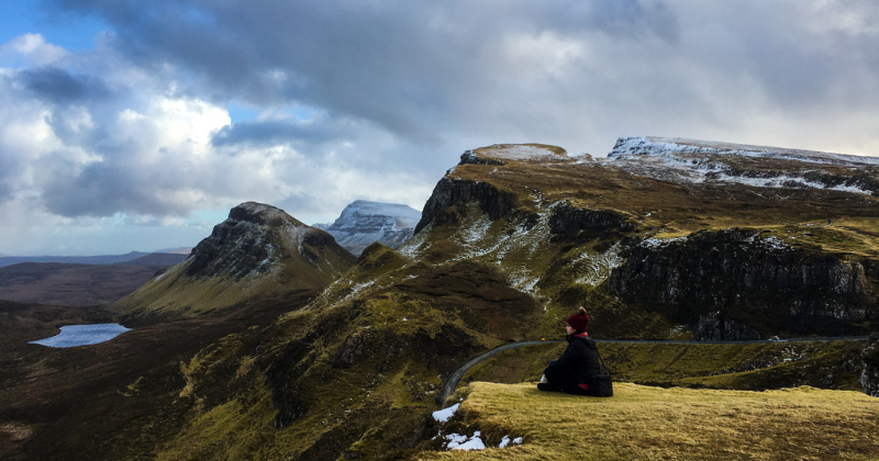A person sitting on a cliff's edge with a view of mountains