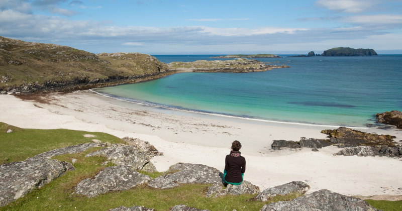 a woman sitting on a rock overlooking a beautiful beach