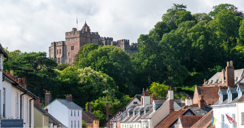 A historic castle overlooks charming homes nestled among lush greenery under a cloudy sky. Perfect for exploring UK heritage.