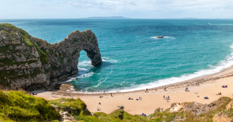 A stunning coastal view featuring a natural rock arch, sandy beach, and turquoise waters, highlighting the beauty of the UK.