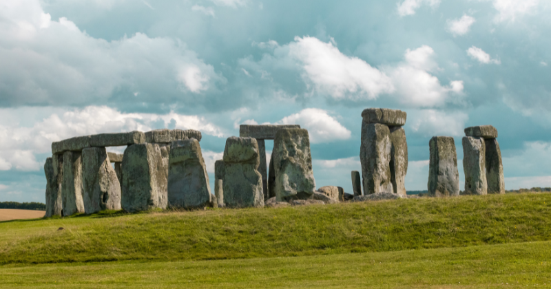 Stonehenge's ancient stone circle set against a cloudy sky and lush green grass, representing a historic UK landmark.