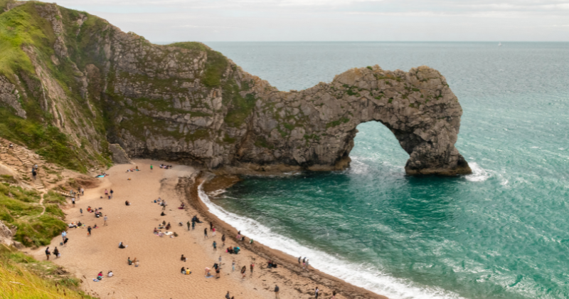 rocky landscape of durdle door with the beach in the bay and the blue sea to the right