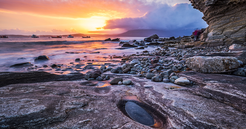 cluster of rocks leading out towards the sea with an orange hue sunset in the background