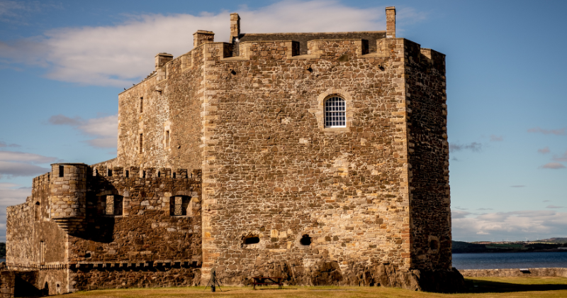 Historic stone castle set against a blue sky, showcasing its medieval architecture and scenic surroundings.