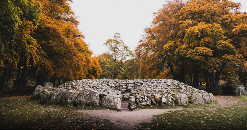 Ancient stone circle surrounded by vibrant autumn trees, creating a serene and historical landscape.