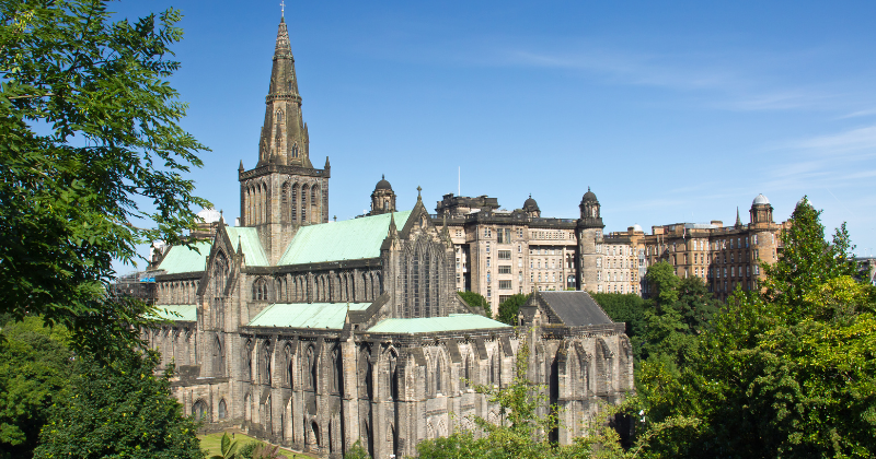 Stunning view of Glasgow Cathedral surrounded by lush trees and historic buildings under a clear blue sky.