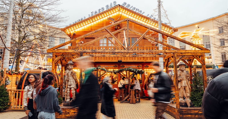 a wooden bar at a christmas market with people walking by