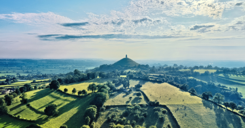 fields of green stretching for miles around with a cloudy blue sky above