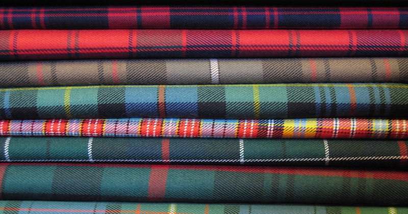 Colorful tartan fabrics stacked neatly, showcasing a variety of patterns and textures, ideal for Scottish-inspired tours.