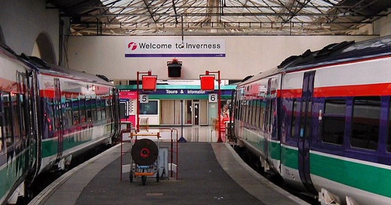 two trains waiting in a station with a sign that says Welcome to Inverness