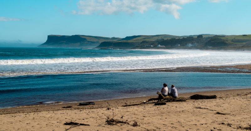 two people sat on the beach looking out to the blue sea