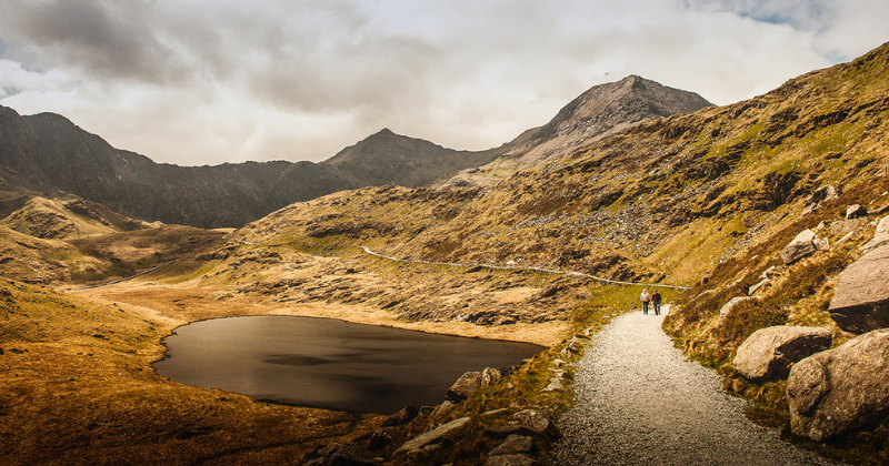 a path by a lake surrounded by mountains