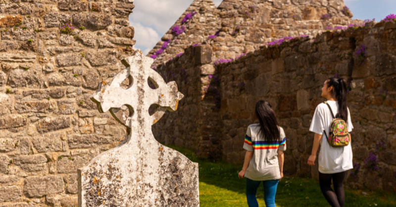 two friends walking through a church garden with a headstone in the foreground