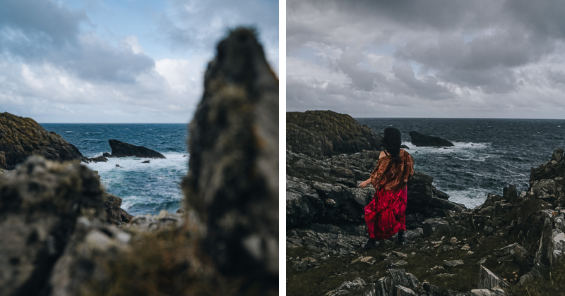 rocky coastal edge with the sea crashing into the stones and a woman looking out at the view