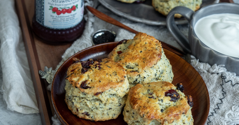 close up image of three scones with jam and cream in the background