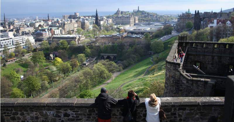 three people stood by a wall overlooking the city of Edinburgh